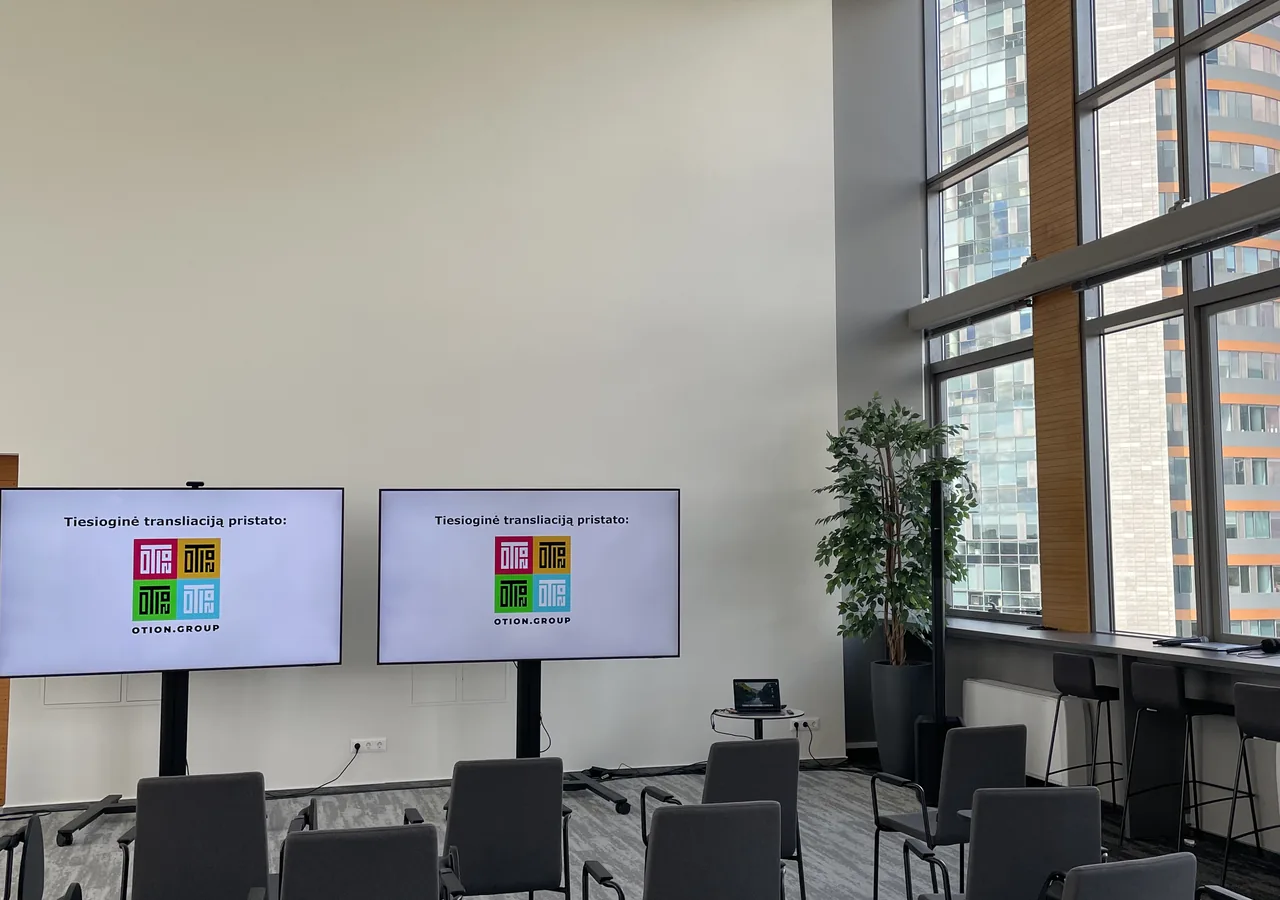 Konferencijų salė su ekranais ir paruošta transliacijos technika